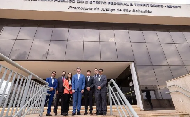 Dois homens de terno posam ao lado de painel da Justiça Eleitoral com a inscrição Eleições 2026