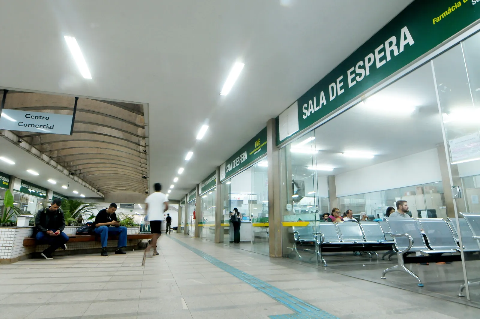 Sala de espera da Farmácia de Alto Custo, com cadeiras e pacientes aguardando atendimento
