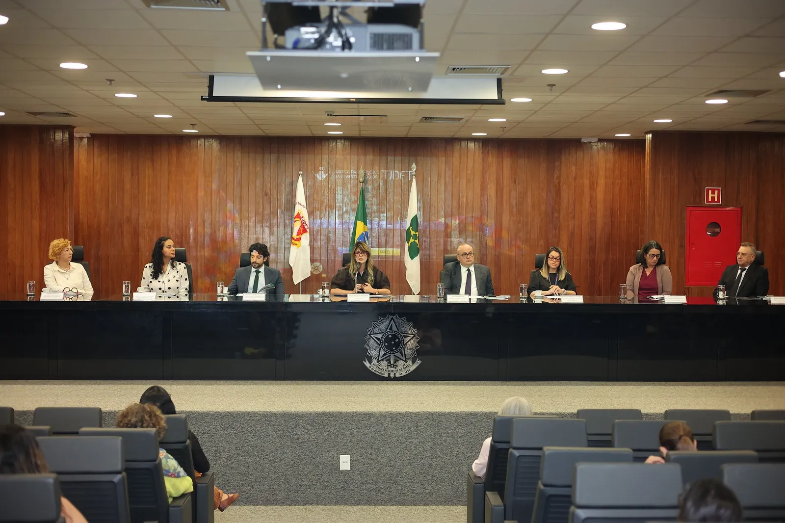 Mesa de abertura de evento no auditório do TJDFT, com oito pessoas sentadas diante de bandeiras