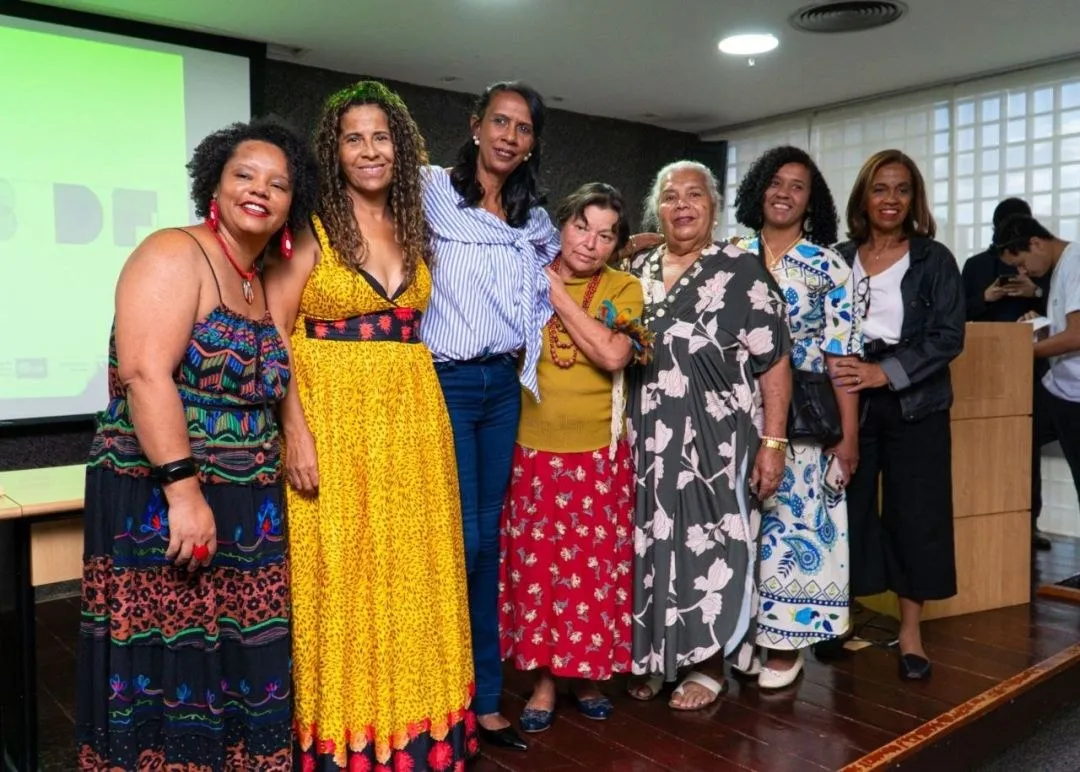 Grupo de mulheres reunidas num auditório, sorrindo para a foto